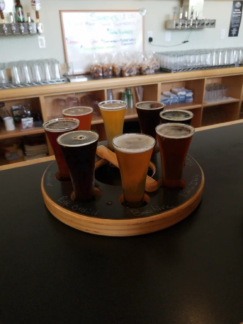 An eight-glass beer flight on a wooden tasting paddle